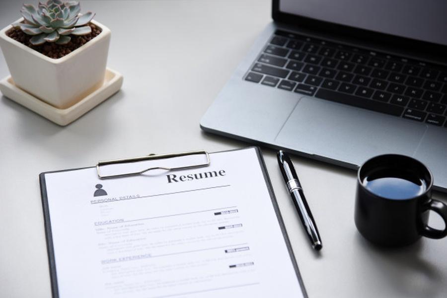 A clipboard containing a resume next to a coffee cup and a laptop