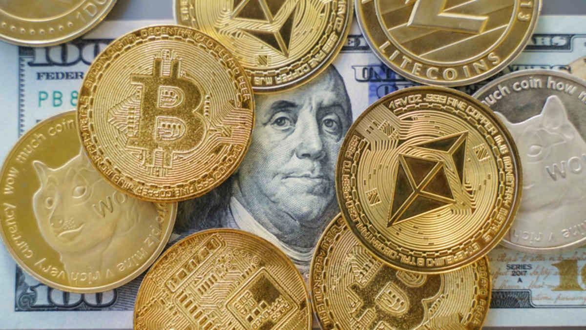 A selection of coins with cryptocurrency signs on them positioned on a hundred dollar bill